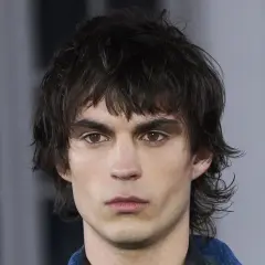 Joven con un moderno corte mullet, cabello oscuro y despeinado, mirada intensa y cejas marcadas.