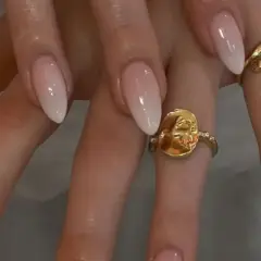 Manos con uñas baby boomer natural, un degradado suave de rosa a blanco. Dos anillos dorados adornan los dedos.