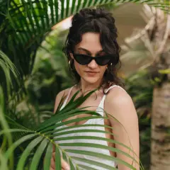 Joven con gafas de sol y traje de baño blanco entre hojas verdes, un ejemplo de moda ecológica.