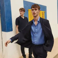 Dos hombres modelan un outfit oficina verano hombre: uno con chaqueta azul marino y camisa de lino, otro con polo oscuro.
