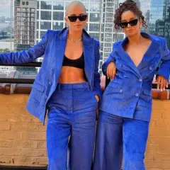 Dos mujeres posan con trajes de pana azul eléctrico, con la ciudad de fondo.