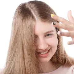Chica sonriente con cabello rubio que se electrifica. Descubre cómo quitar la electricidad del pelo para un look suave.