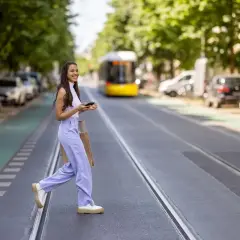 Mujer sonriente cruza la calle con bolsas, disfrutando de su estilo de slow fashion.