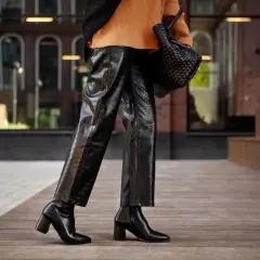 Elegante outfit con botas altas negras, pantalones de cuero texturizado y suéter naranja.