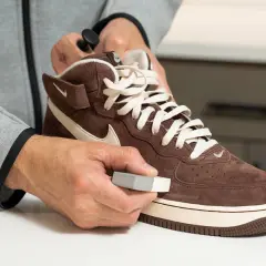 Persona limpia un zapato de ante marrón con un borrador, demostrando que el ante se puede mojar y limpiar.
