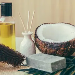Aceite de coco para el pelo, junto a un coco partido, jabón y un cepillo.