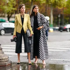 Dos mujeres con estilo muestran cómo vestir en otoño en España: una con blazer amarillo y pantalón culotte de cuero, la otra con abrigo de pata de gallo.