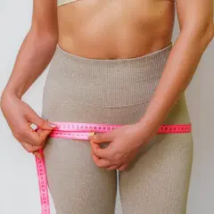 Mujer midiendo su cintura con cinta métrica rosa, enfocándose en la zona de los **hip dips**.