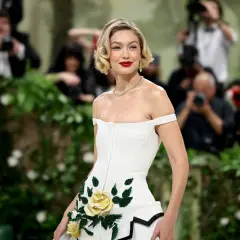 Gigi Hadid deslumbrante en la Met Gala, con un vestido blanco adornado con rosas amarillas y verdes.