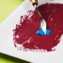 Mezclando azul con rojo para descubrir como se hace el color granate. Una espátula recoge pintura azul sobre una base roja.