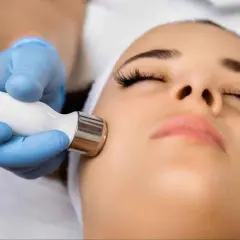 Un rostro recibe un tratamiento facial con exosomas, aplicado con un dispositivo de mano por un profesional con guantes azules.