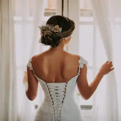 Novia con un juvenil recogido de boda adornado con flores, luciendo su espalda con un corsé de encaje.