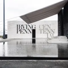 Reflejos en el agua de la entrada a la celebración del centenario de Irving Penn, con un toldo gris sobre la estructura.