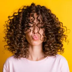 Mujer con pelo corto rizado y labios en forma de beso, sobre fondo amarillo.