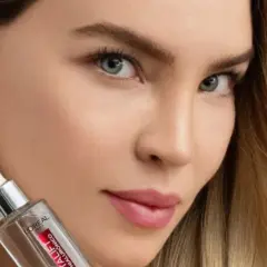 Mujer con cabello rubio y joyas brillantes sostiene un frasco de sérum, parte de su rutina de cuidado de la piel.