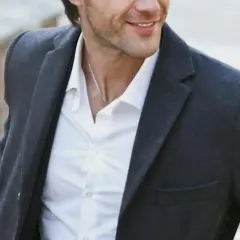 Hombre sonriente con chaqueta gris y camisa blanca, luciendo un estilo look smart casual.
