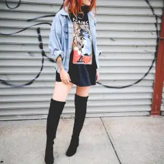 Chica con botas altas para bajitas, chaqueta vaquera y camiseta gráfica, posando frente a una pared de garaje con grafitis.