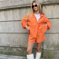 Mujer con conjunto naranja, gafas de sol y botas blancas. Se ve muy comfy y lista para pasear.