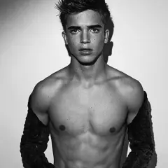 Joven modelo hombre con mirada intensa, torso descubierto y mangas oscuras.