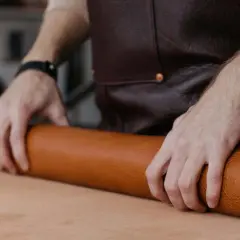 Manos de artesano desenrollando un rollo de cuero, mostrando la textura y el color natural del material. Se pregunta de que esta hecho el cuero.
