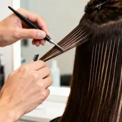 Manos expertas aplican mechas babylight con precisión, creando un efecto natural y luminoso en el cabello castaño.