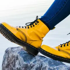 Botas amarillas de charol, con cordones negros, pisan una roca. Las botas de piel ceden ante la aventura.