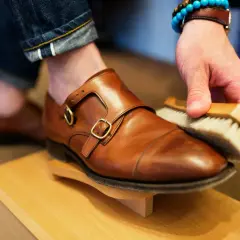 Hombre cepillando un zapato de piel marrón, parte de como limpiar zapatos de piel.