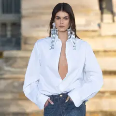 Mujer con camisa blanca desabrochada y vaqueros, luciendo grandes pendientes brillantes.