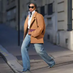 Mujer con abrigo camel, camisa blanca y jeans anchos, luciendo un bolso morado. Su estilo es muy aesthetic.
