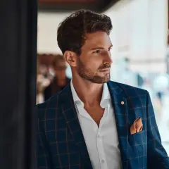 Un invitado boda hombre sin traje, con chaqueta a cuadros, camisa blanca y pañuelo naranja.
