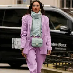 Una mujer luce un traje lila y un suéter azul pálido, demostrando que el azul es un color que combina con el lila.