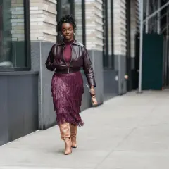Mujer con falda de flecos burdeos y chaqueta a juego, luciendo botas altas. Un ejemplo de cómo combinar zapatos burdeos mujer con estilo.