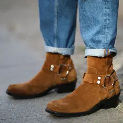 Botas de gamuza marrón con hebillas y jeans doblados. La piel girada de las botas contrasta con el denim.