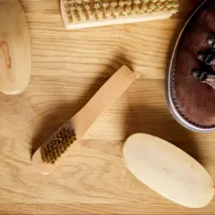 Cepillos y bota de piel de ante marrón sobre madera.