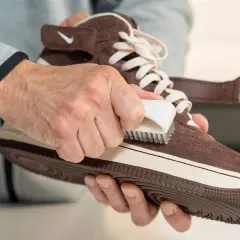 Man limpiando serraje de una zapatilla marrón con un cepillo blanco.