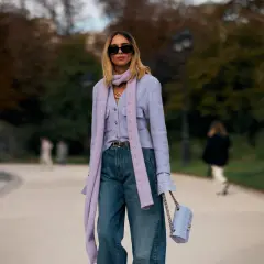 Mujer con look elegante con vaqueros, chaqueta lila, bufanda y bolso a juego.
