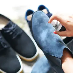 Aplicando spray protector a unas botas de terciopelo azul. Aprende como limpiar botas de terciopelo para mantenerlas como nuevas.
