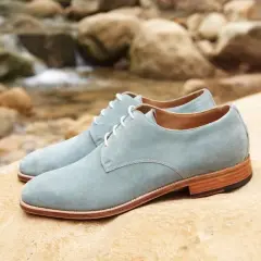 Zapatos de ante azul claro con cordones blancos, descansando sobre rocas junto a un arroyo. ¡Qué ante en zapatos!