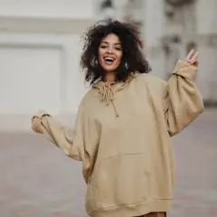 Mujer sonriente con pelo rizado, luciendo un cómodo estilo oversize en sudadera beige.