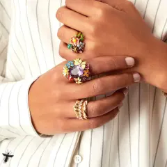 Manos adornadas con anillos florales coloridos y un reloj dorado, luciendo un estilo suot studio.
