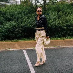 Mujer con elegante **pantalón beige** de talle alto, camisa negra brillante y bolso blanco.