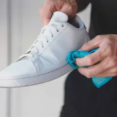 Manos limpiando las gomas de unas zapatillas blancas con un paño azul. Un detalle para saber como limpiar las gomas de las zapatillas y dejarlas como nuevas.