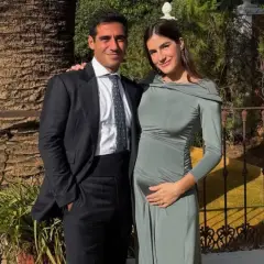 Pareja sonriente, él con traje oscuro, ella con vestido verde ceñido, acariciando su vientre. Blanca Llandres, radiante, espera un bebé.