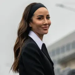 Mujer con peinado con diadema y pelo suelto, luciendo un traje negro y camisa blanca.