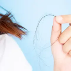 Mano sujetando mechón de pelo, mostrando preocupación por la caída. ¿En qué época del año se cae más el pelo?