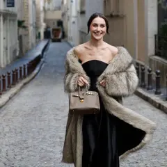 Elegante mujer con abrigo de pelo y bolso, lista para una boda en otoño.