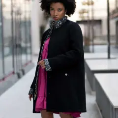 Mujer con estilo urbano y moda oversize, luce un vestido rosa vibrante bajo una chaqueta negra con detalles de lunares.