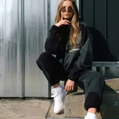 Chica con estilo moderno ropa, gafas de sol y zapatillas blancas, sentada en escalones de hormigón frente a una pared de metal.