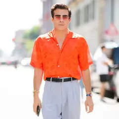 Hombre con camisa naranja estampada y pantalones grises, luciendo un elegante french tuck.