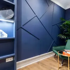 Un sillón verde menta contrasta con la pared azul oscuro. Una planta y libros descansan sobre una mesa dorada.